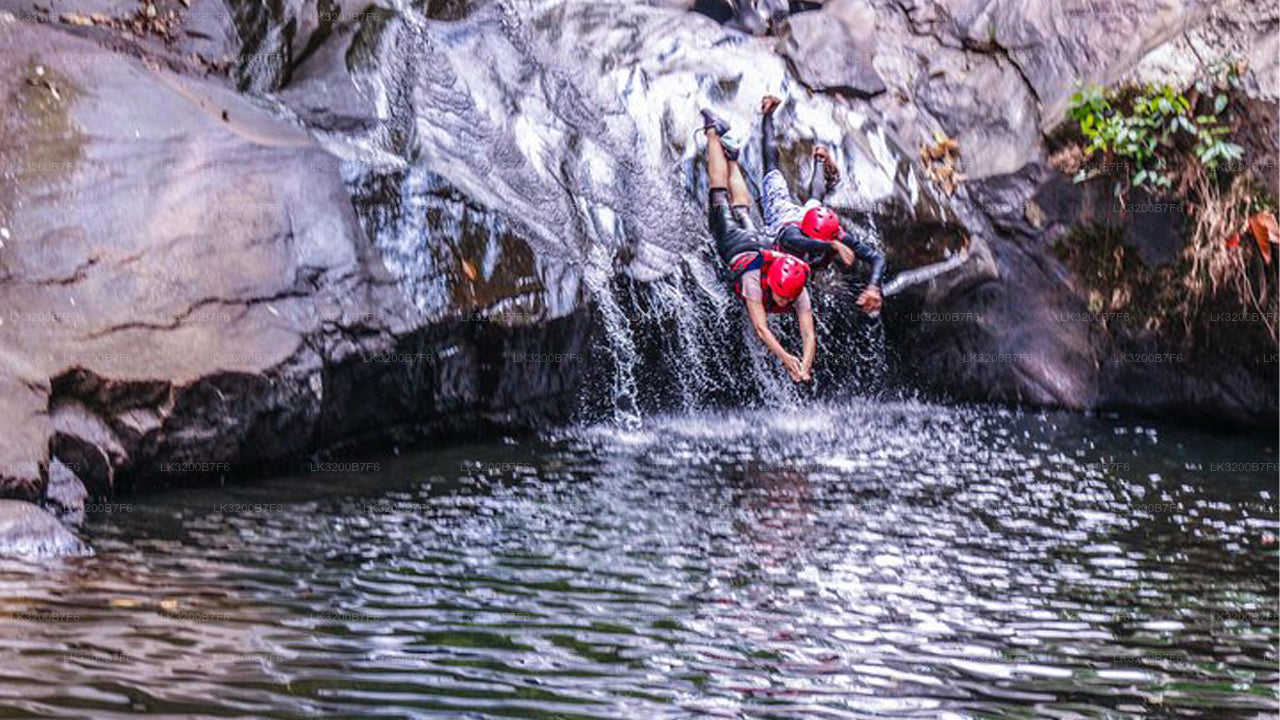 Person in a red helmet climbing a rocky waterfall into a pool of water.