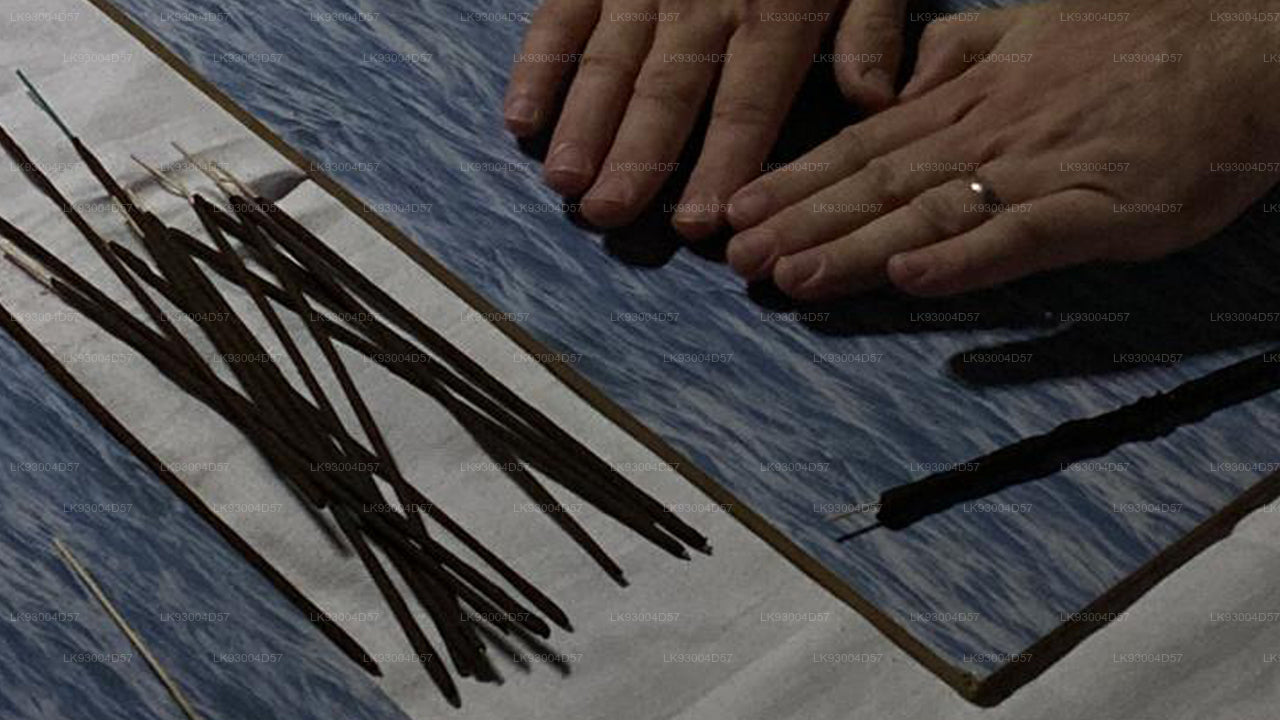 Close-up of hands with a ring on a textured surface with black sticks.