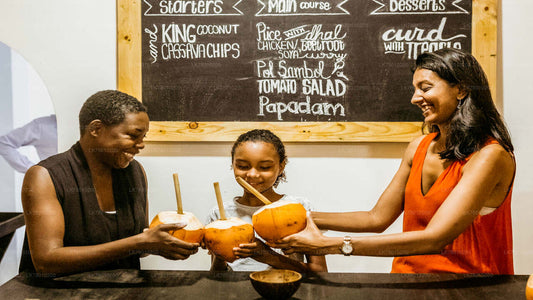 Three people participating in a Sri Lankan cooking class, standing around a table with cooking ingredients and utensils, with a blackboard menu in the background.